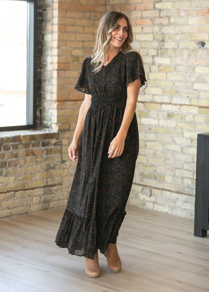 Black floral leaf maxi dress with flowing tiered hem and ankle-length silhouette on a 5'7" model.