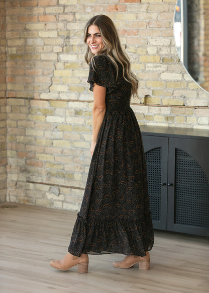 Black floral leaf maxi dress with flutter sleeves, smocked waist, and tiered hem, shown from the back.