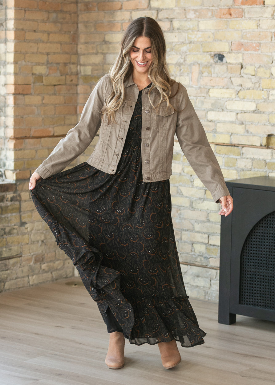Black floral leaf maxi dress layered with a taupe denim jacket and neutral ankle boots.