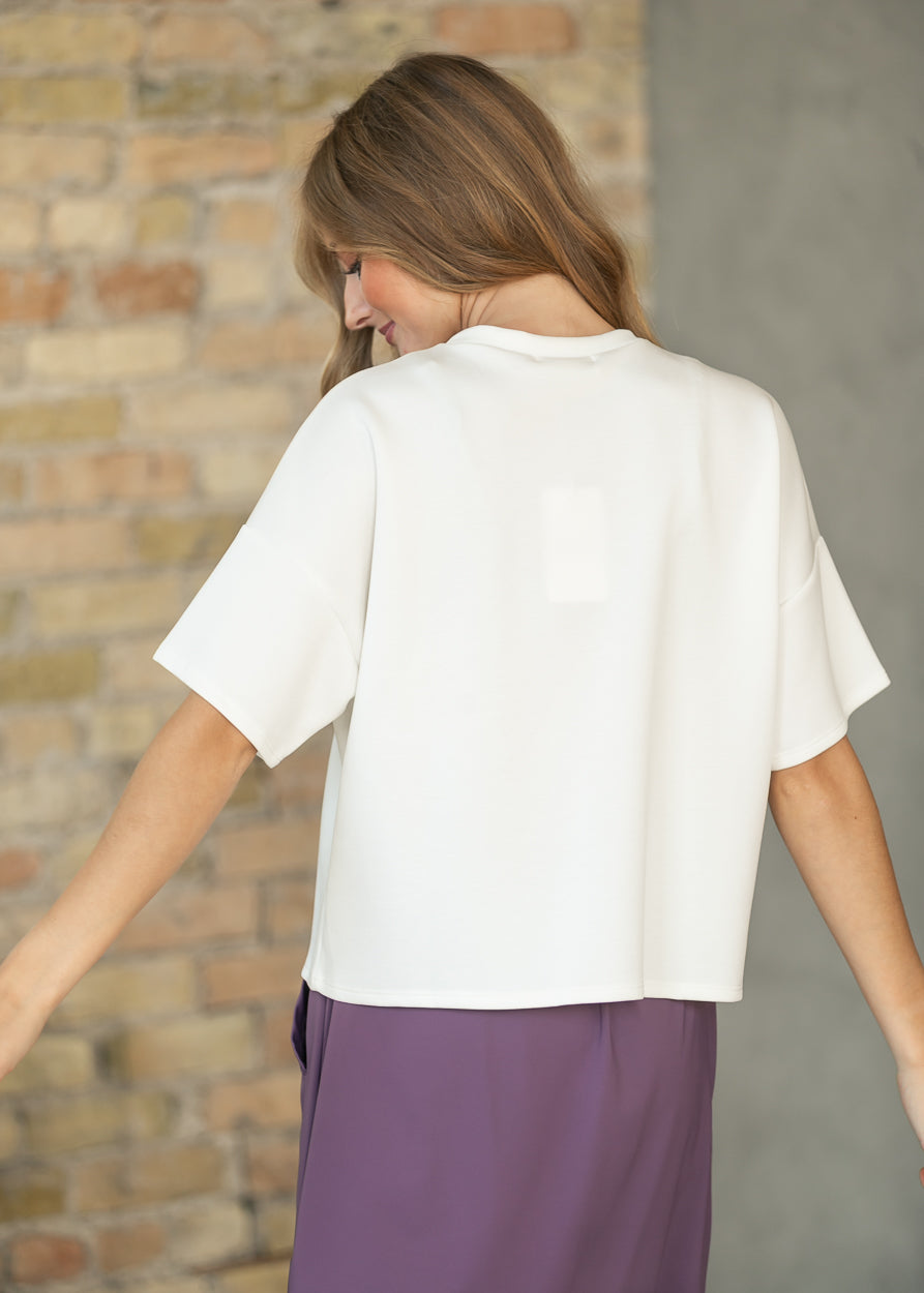 Ivory short sleeve scuba top from the back, styled with a purple skirt.
