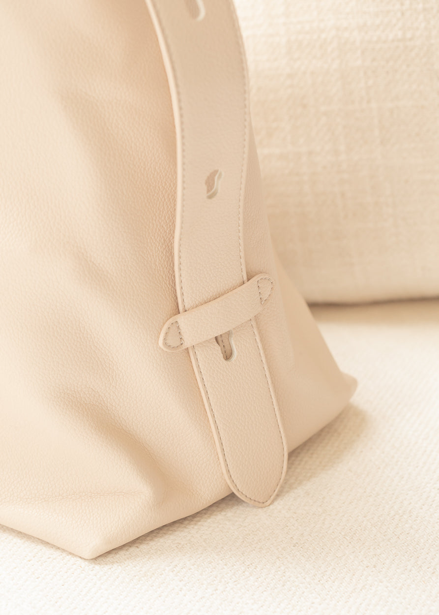 Close-up of ivory tote bag with adjustable shoulder strap and pebbled faux leather texture.