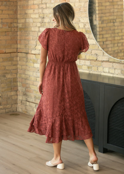 Rust jacquard floral midi dress from the back, showing flutter sleeves, gathered waist, and layered ruffle hem.