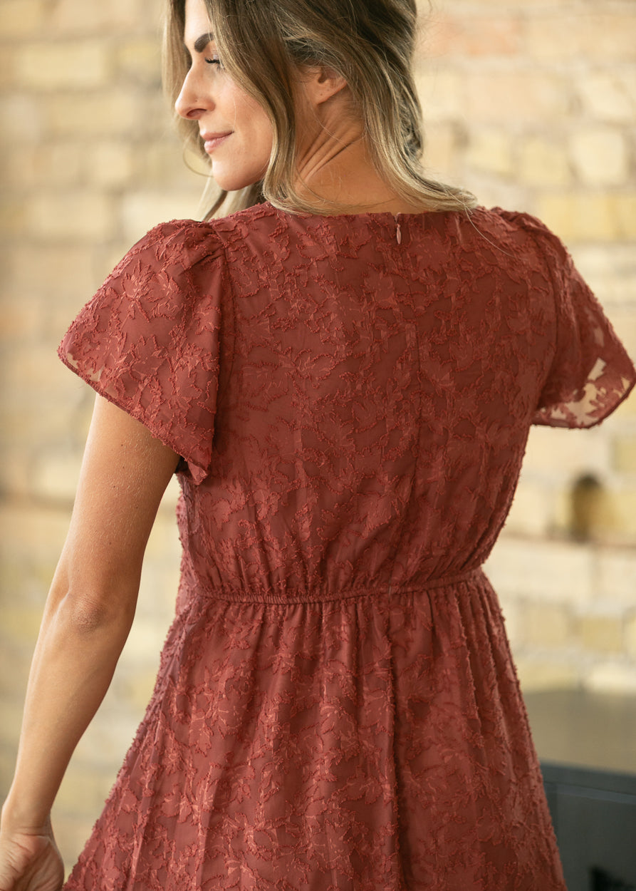 Close-up of rust floral jacquard dress back with textured fabric, flutter sleeves, and gathered waist.