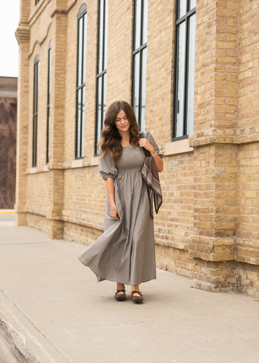 Brown chambray maxi dress showing its semi-fitted bodice and long flowing silhouette.