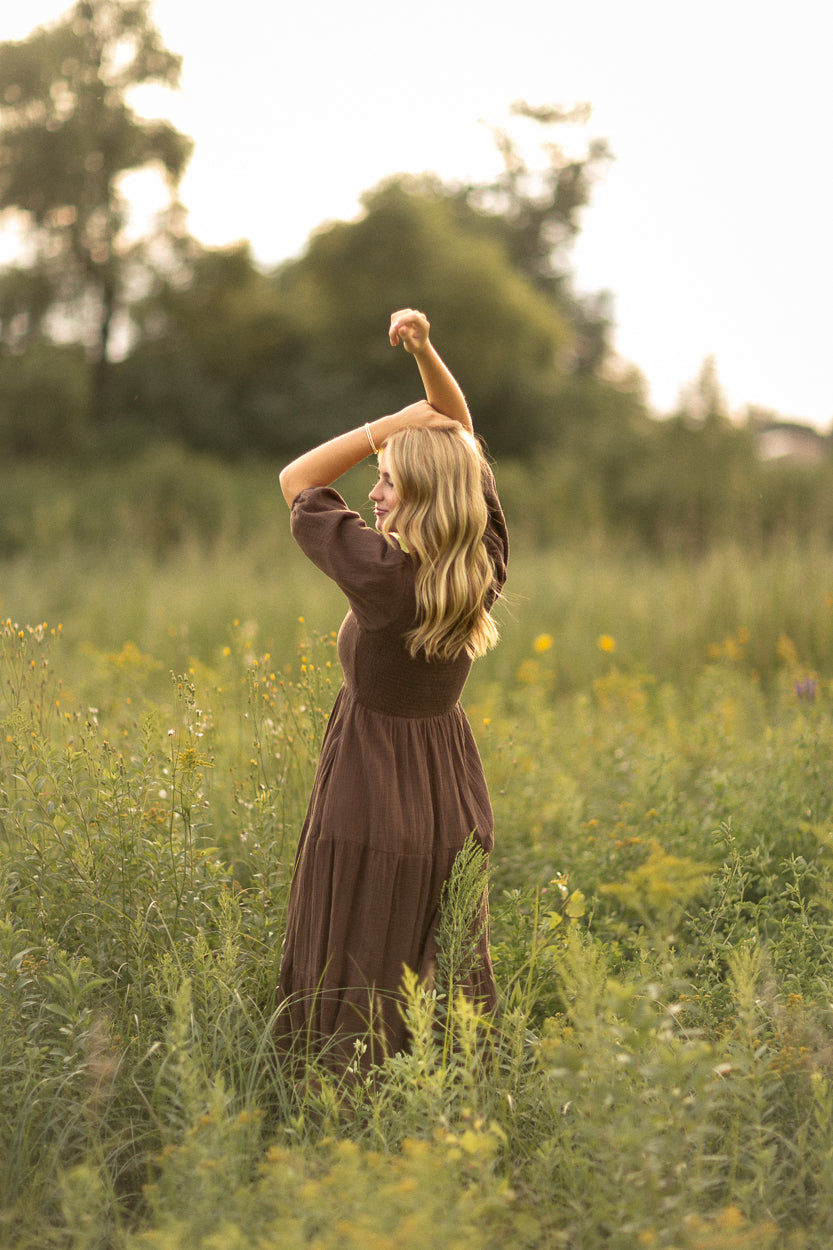 Chocolate brown maxi dress with short sleeves and a flowy skirt styled outdoors at sunset.
