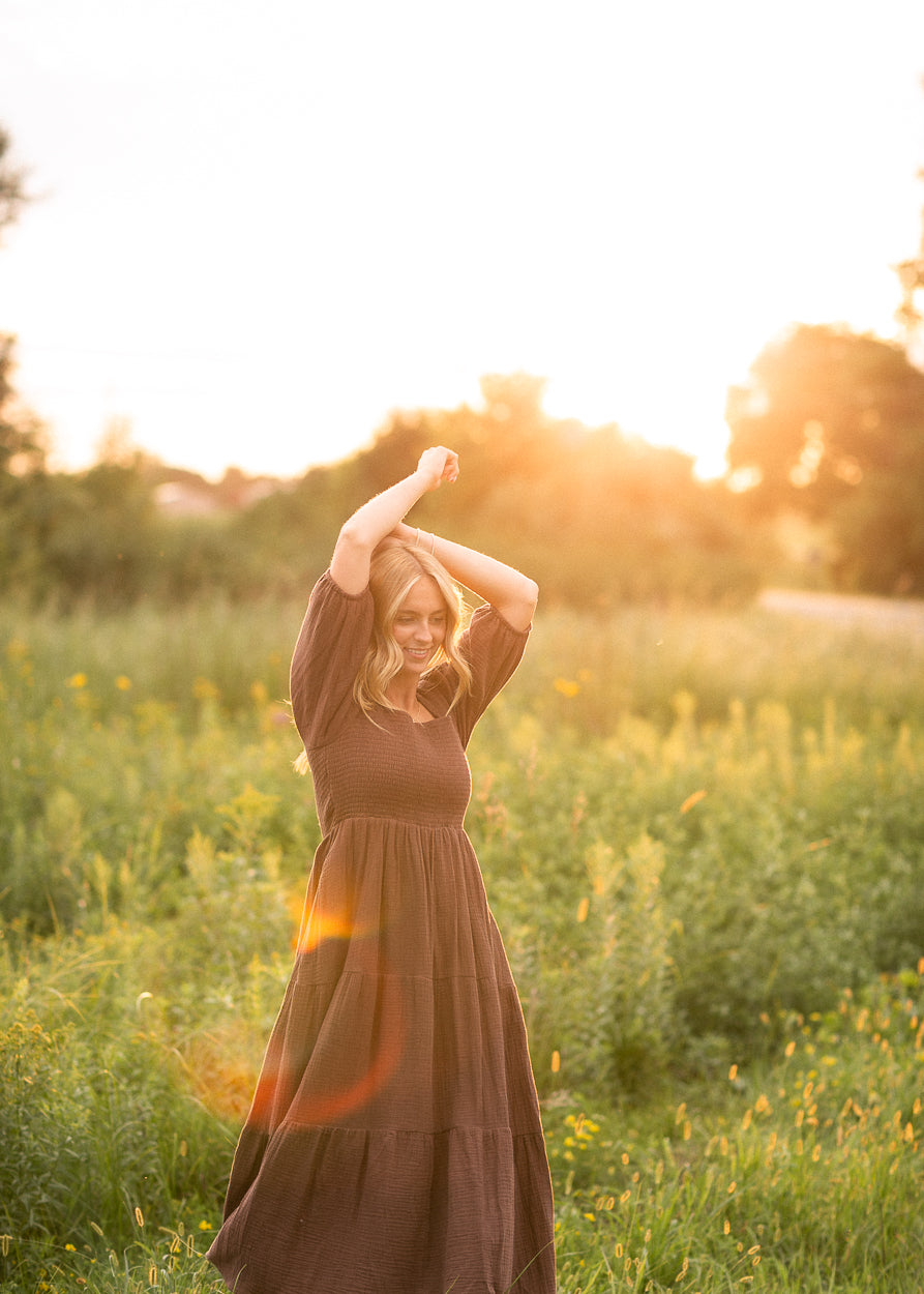 Chocolate Kayleen gauze maxi dress photographed in a sunlit meadow with its skirt in motion.