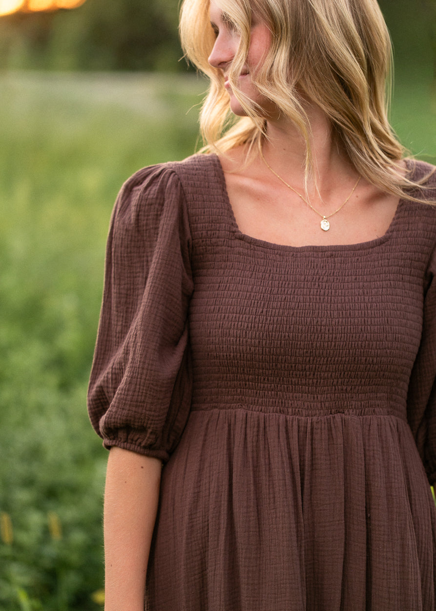 Chocolate brown cotton maxi dress with smocked bodice, short sleeves, and softly gathered skirt.