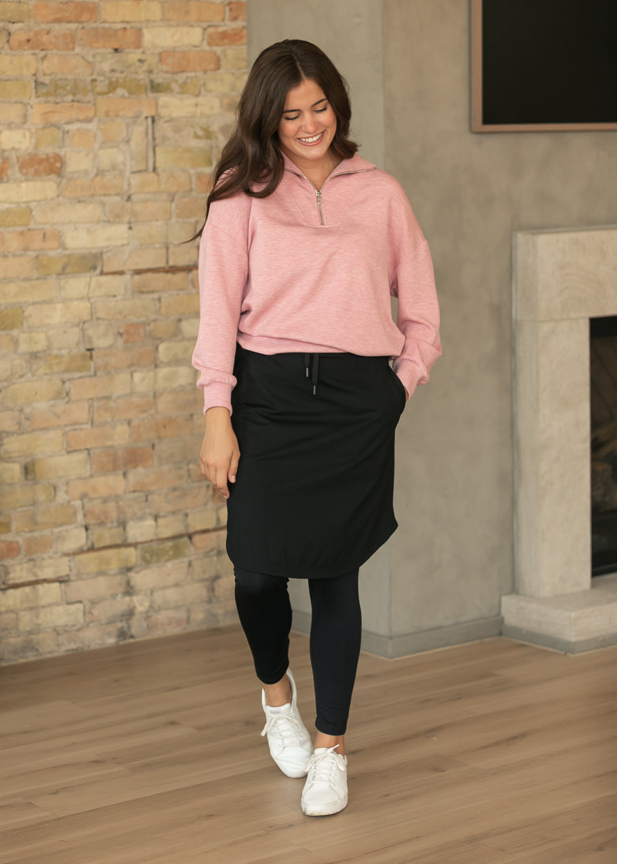 Black athletic skirt with built-in leggings styled with a pink quarter-zip and white sneakers.