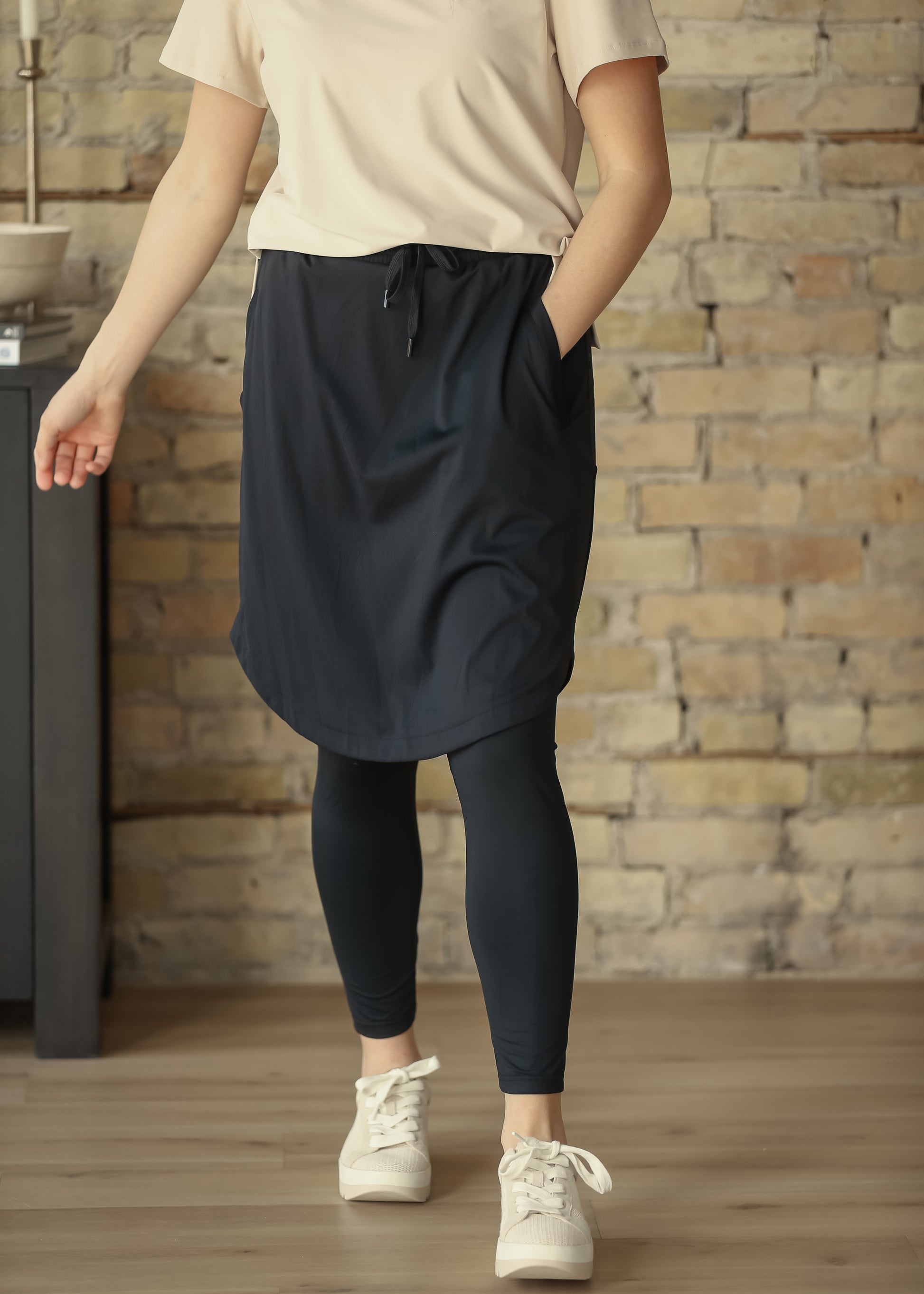 Front view of black athletic skirt with built-in leggings, drawstring waist, and side pockets.