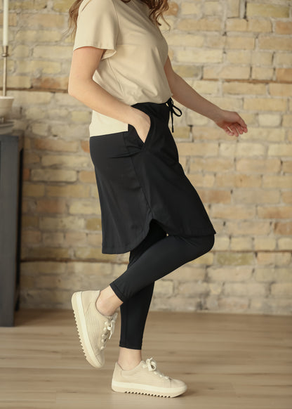 Black Kenedi sport skirt with leggings styled with a beige short sleeve top and neutral sneakers.