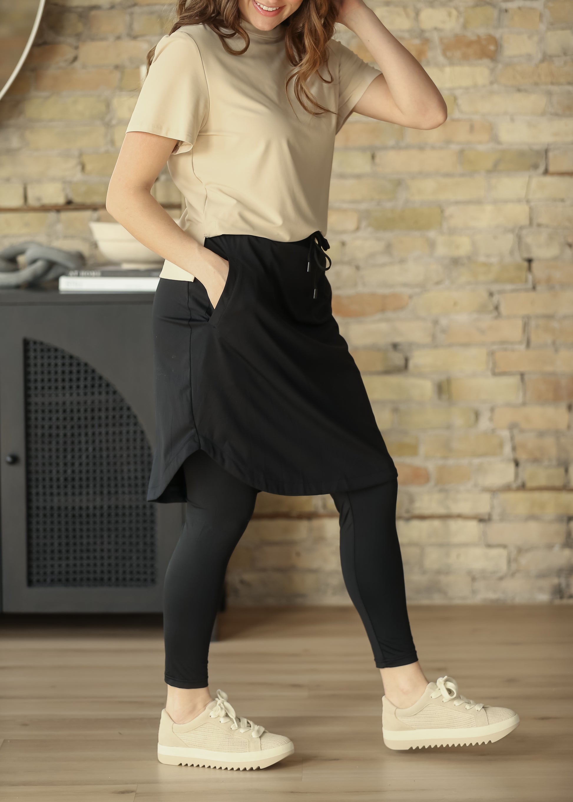 Black sport skirt with built-in leggings shown in motion with a beige tee and sneakers.