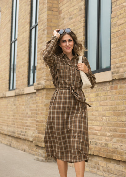 Brown plaid midi dress with long sleeves and defined tie waist, photographed beside a brick building.