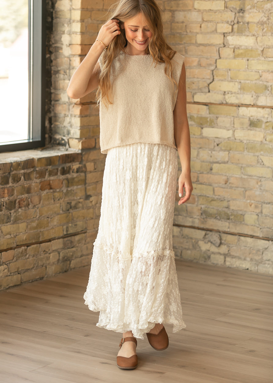 Beige sleeveless knit sweater top styled with an ivory lace maxi skirt and brown flats.