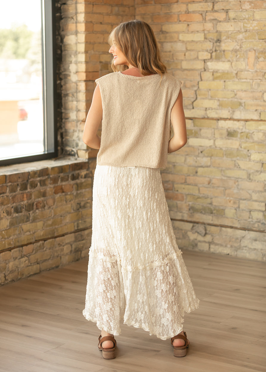 Back of ivory floral lace midi skirt showing the flowing tiered hem, styled with a beige sleeveless knit top.