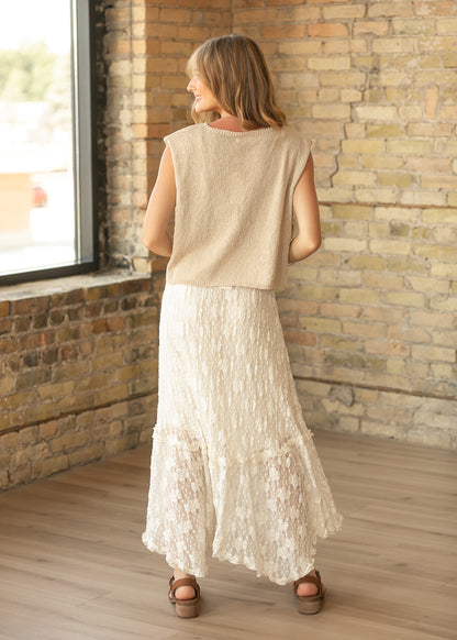 Back of ivory floral lace midi skirt showing the flowing tiered hem, styled with a beige sleeveless knit top.