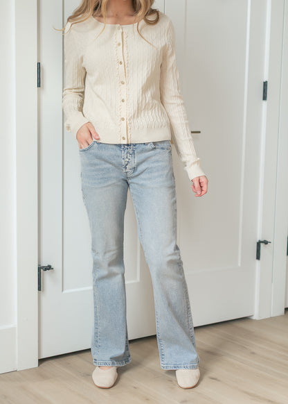 Person wearing a cream cardigan and light blue jeans indoors.