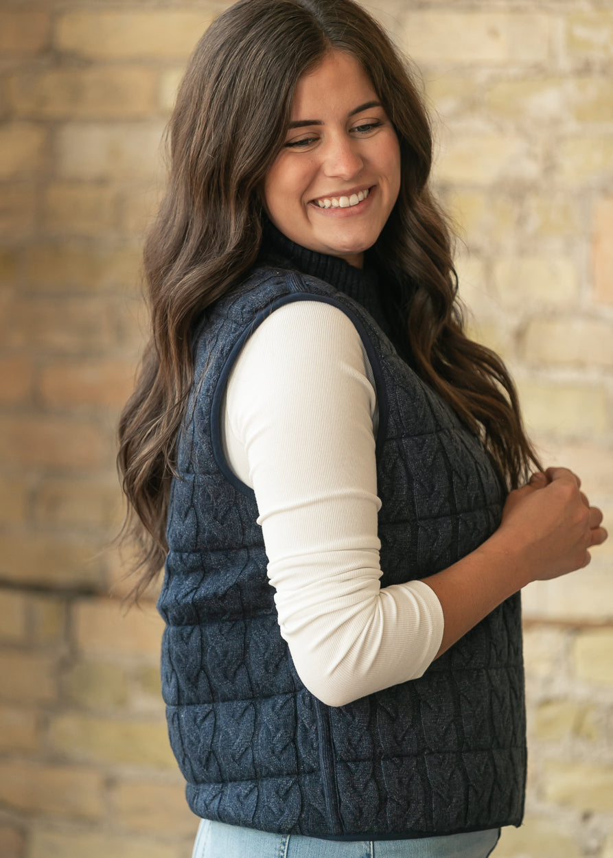 Side view of navy cable-knit vest showing semi-fitted shape, ribbed collar, and quilted texture.