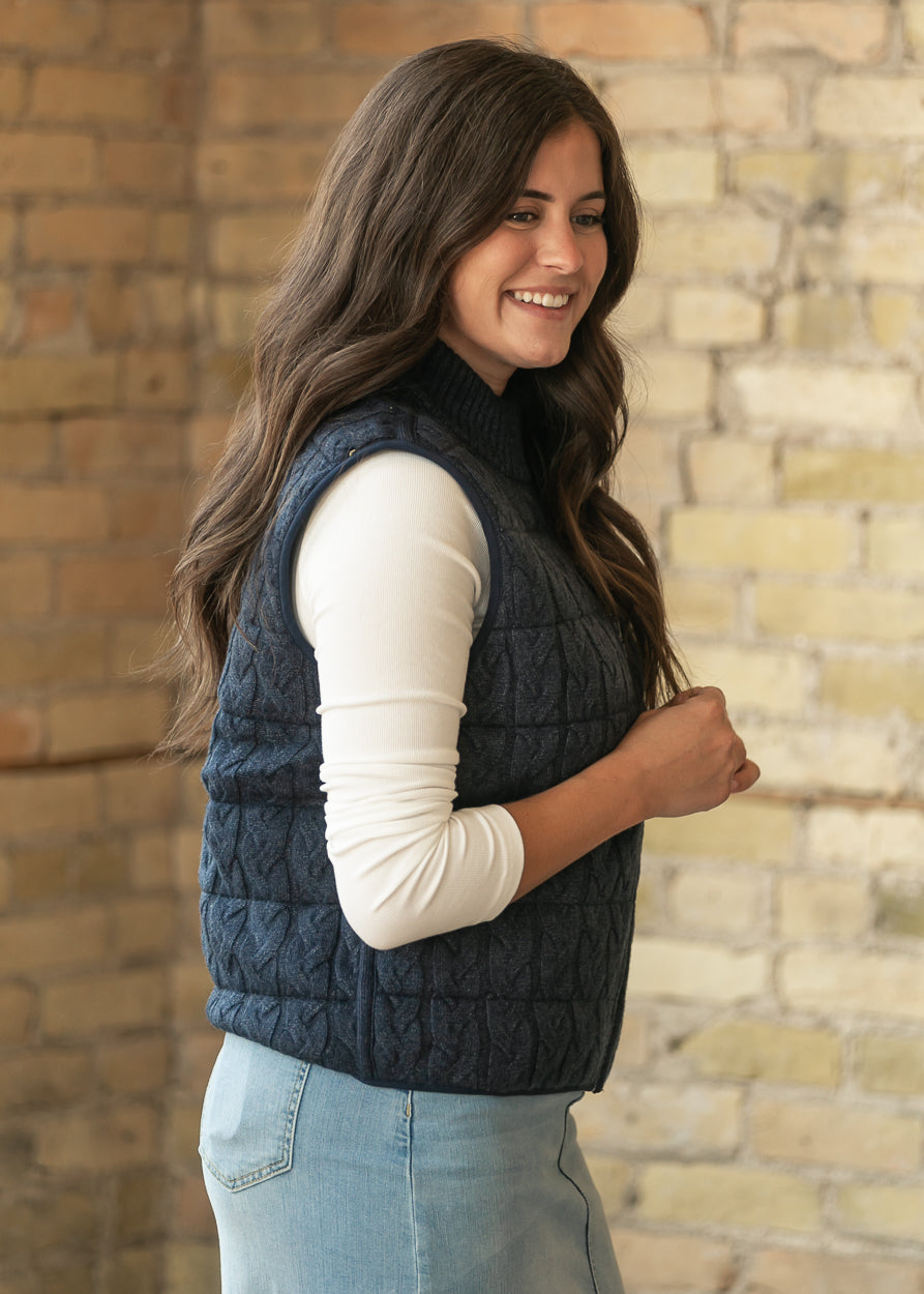 Navy reversible vest in side profile, layered over a cream top and light wash denim skirt.