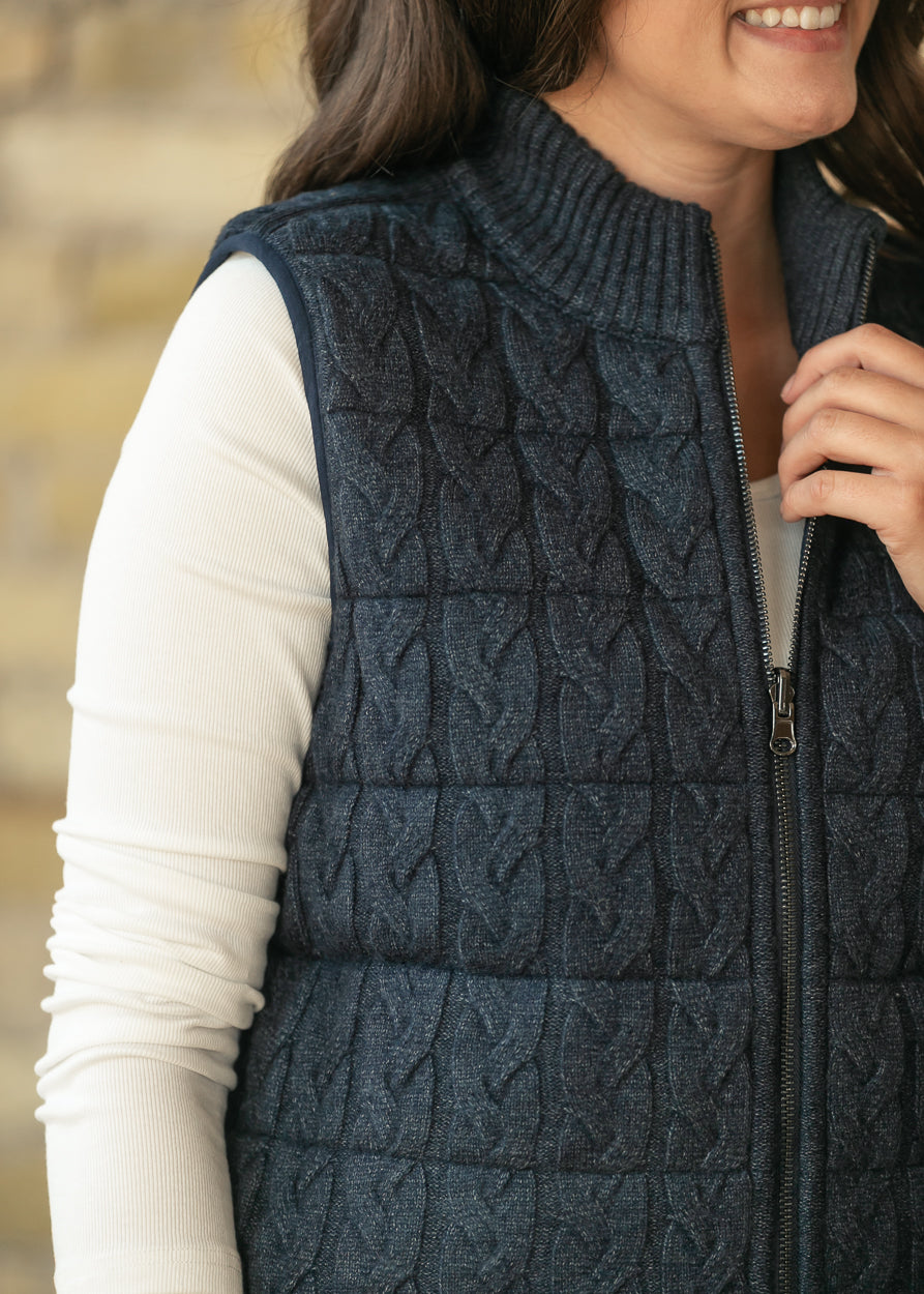 Close-up of navy cable-knit quilted vest showing ribbed mock neck, zipper, and textured front.