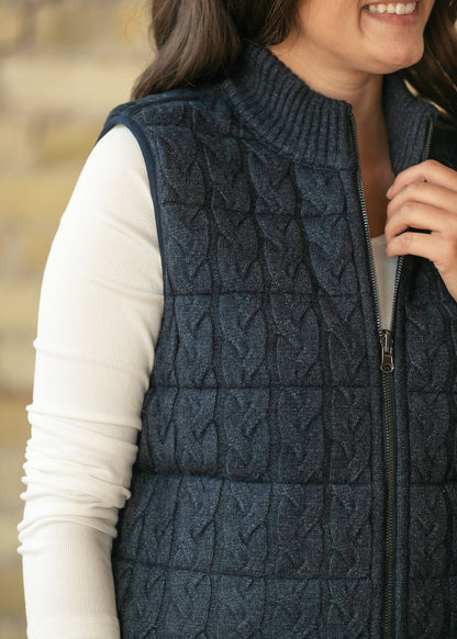 Close-up of navy cable-knit quilted vest showing ribbed mock neck, zipper, and textured front.