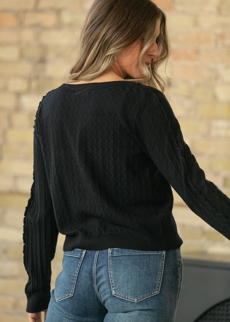 Back of black textured cardigan showing allover knit texture, long sleeves, and ribbed hem.