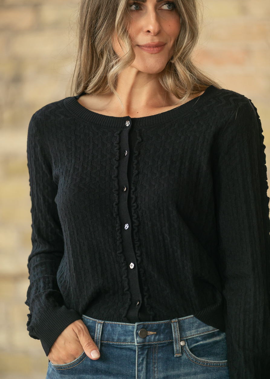 Black textured long sleeve cardigan with button front and delicate trim, styled with medium wash jeans.