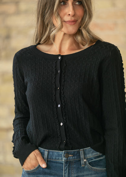 Black textured long sleeve cardigan with button front and delicate trim, styled with medium wash jeans.
