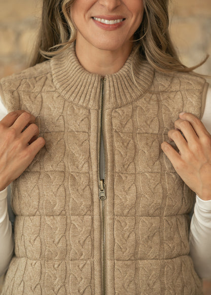 Close-up of taupe cable-knit vest showing ribbed mock neck, textured quilting, and full zipper.