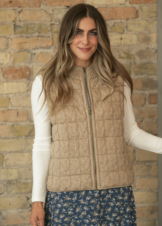 Taupe sleeveless reversible vest showing cable-knit texture, ribbed mock neck, and full-zip front.