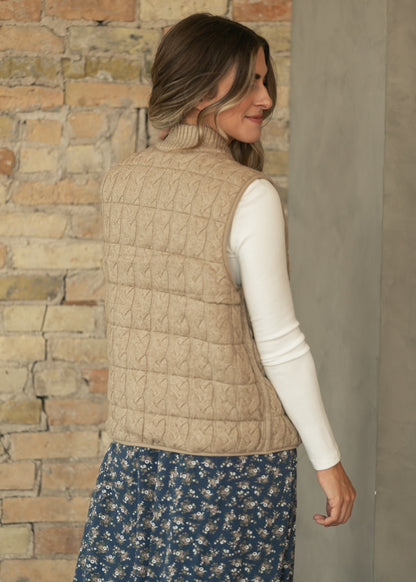 Back of taupe reversible cable-knit vest layered over a cream long sleeve top and navy floral skirt.