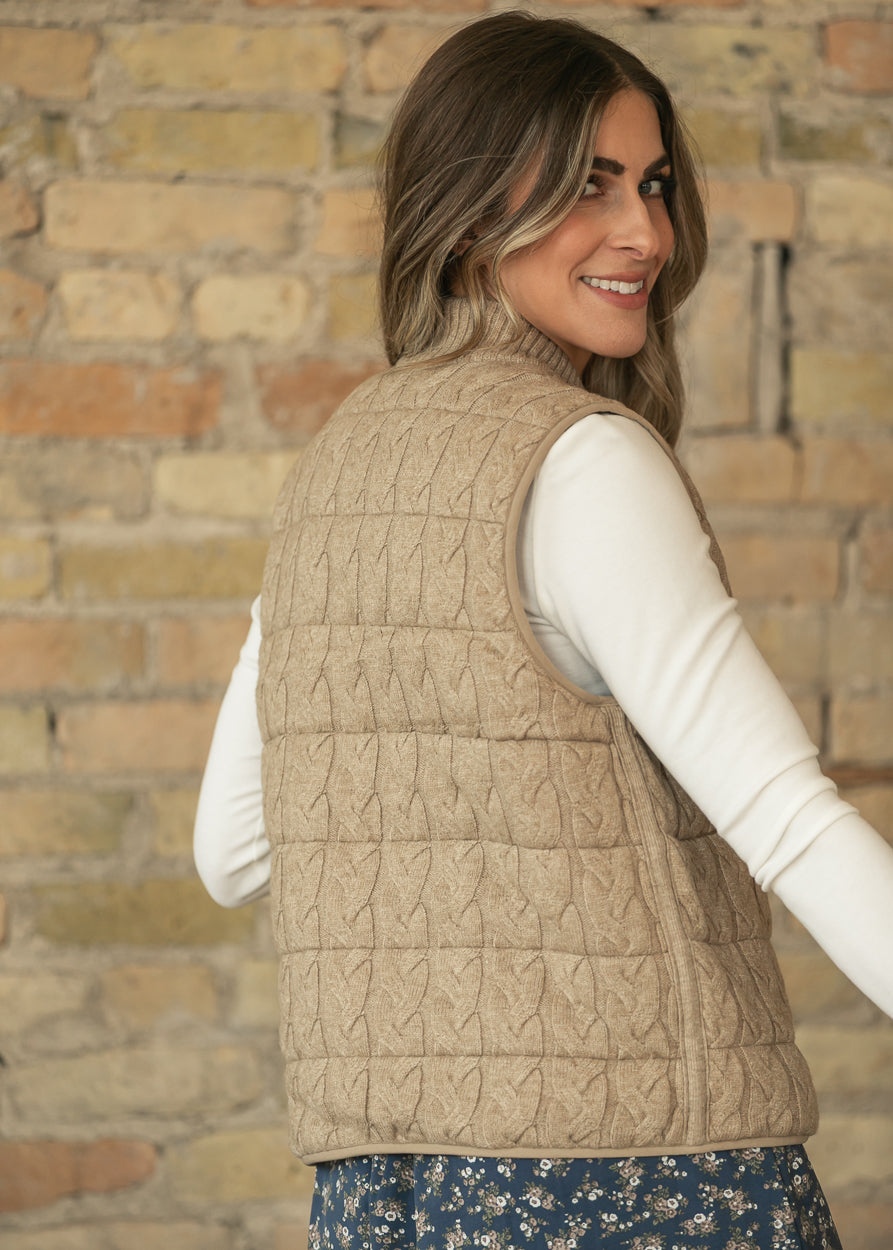 Back three-quarter view of taupe sleeveless vest showing cable-knit texture and hip-length hem.