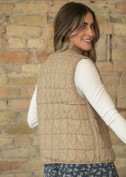 Back three-quarter view of taupe sleeveless vest showing cable-knit texture and hip-length hem.