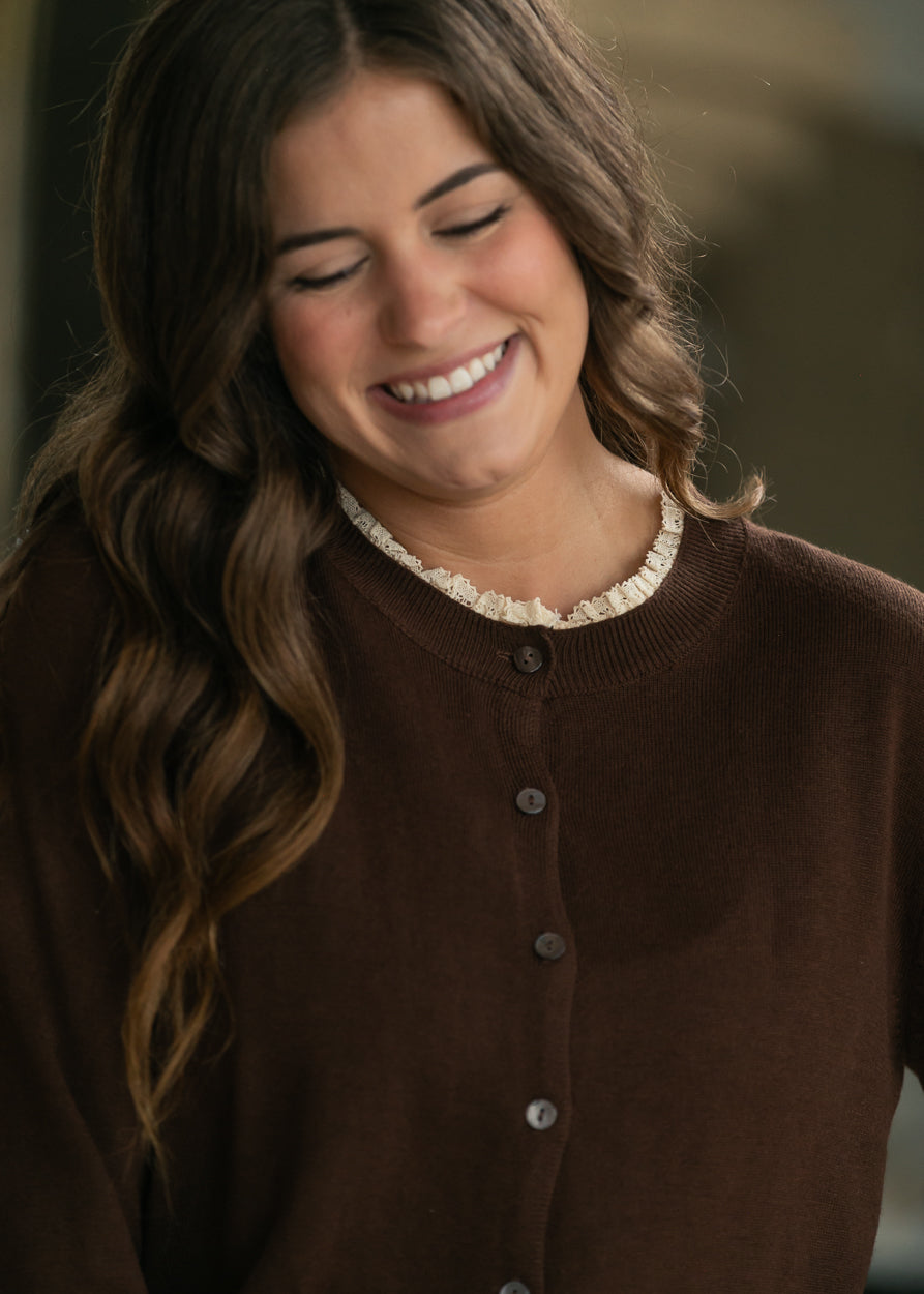 Close-up of chocolate button-up cardigan showing cream lace neckline trim and functional buttons.