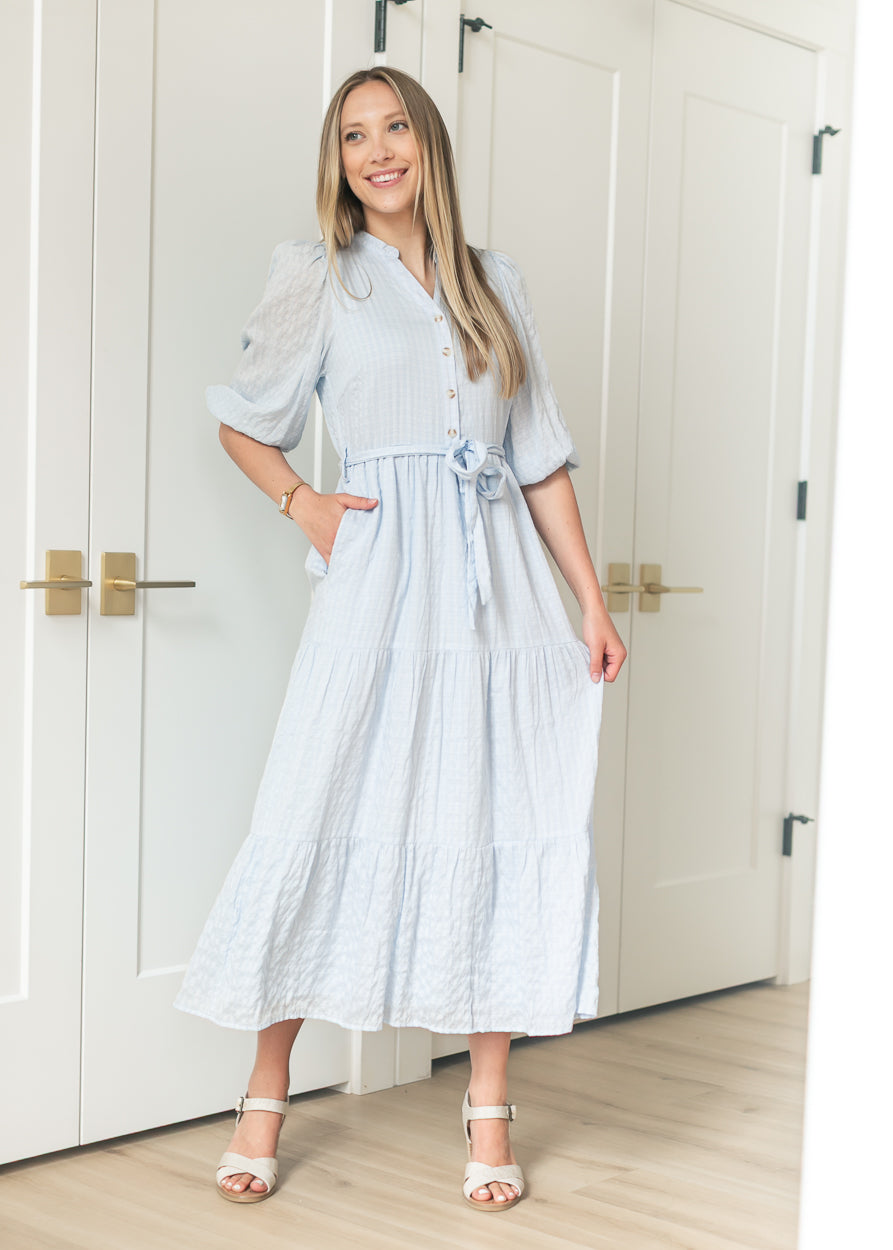 Front view of light blue tiered maxi dress with balloon sleeves and button-front placket, styled with heeled sandals.