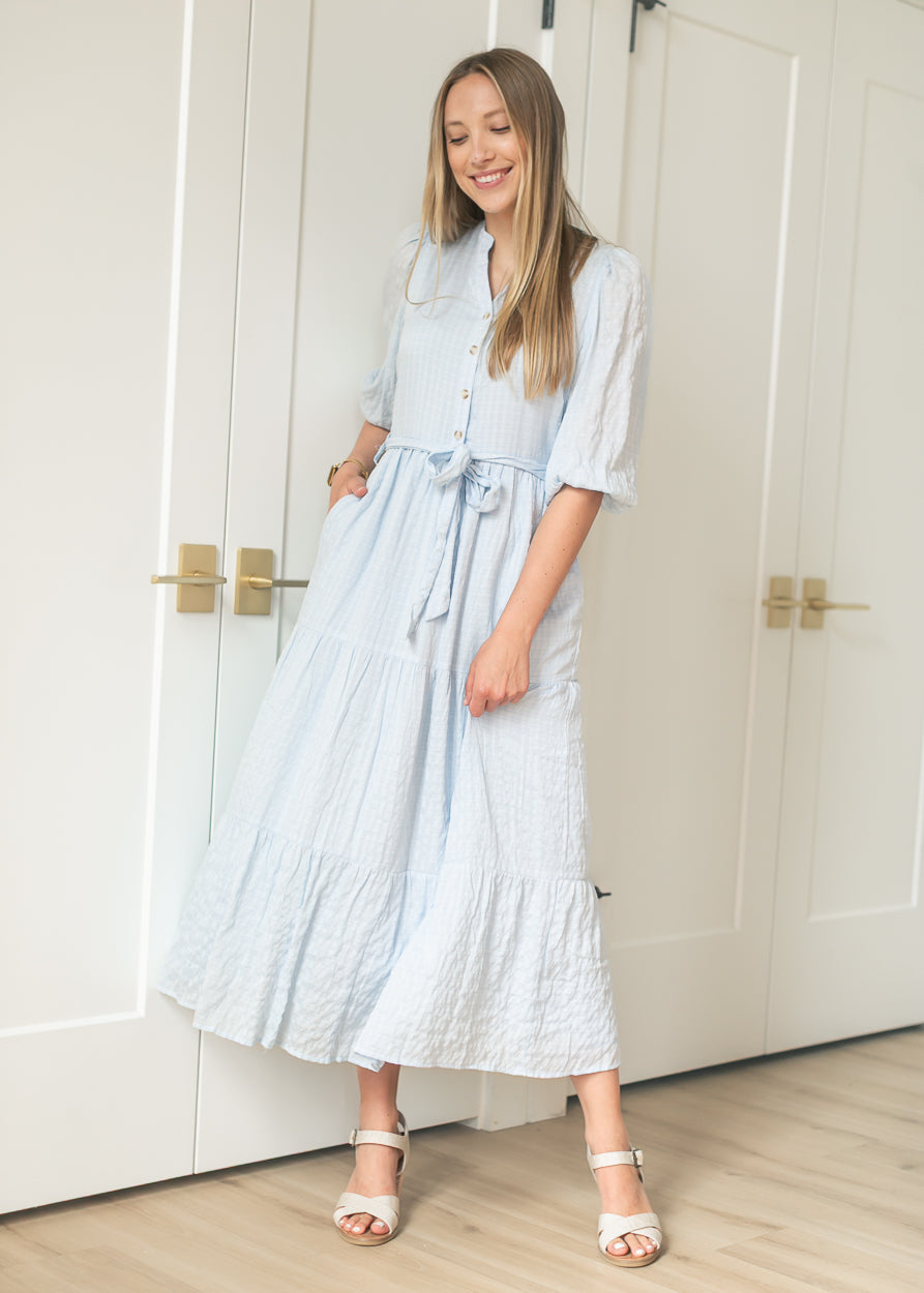 Light blue waist tie maxi dress worn with hand in side pocket, styled with cream heeled sandals.