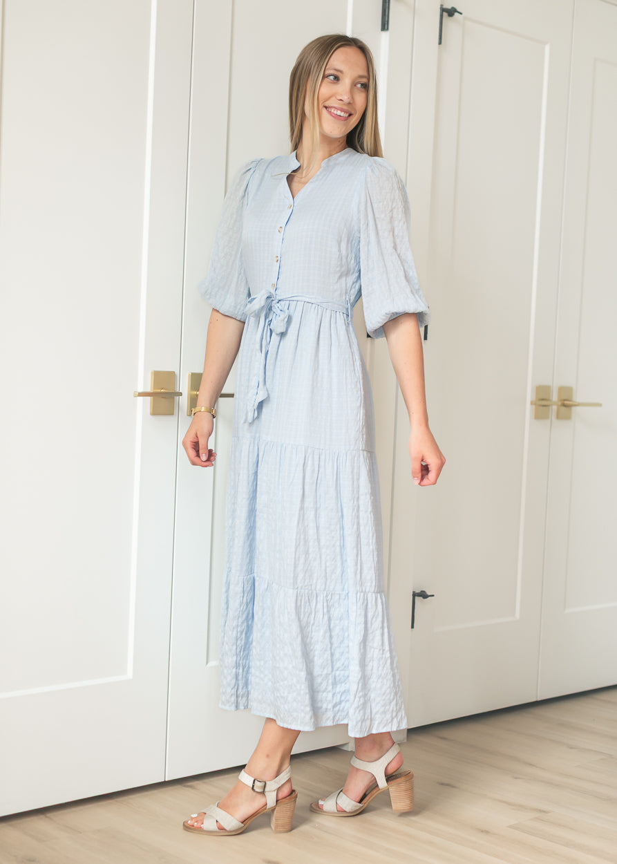 Light blue tiered maxi dress with button-front placket and self-tie waist, front view with heeled sandals.