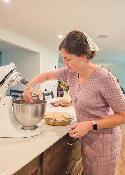 Woman in a kitchen using a stand mixer with a pie in the background
