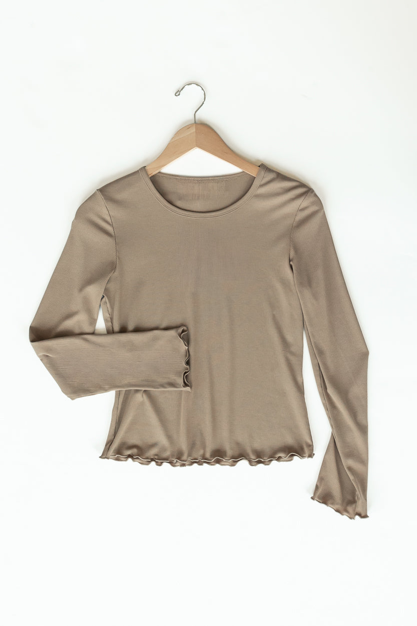 A taupe long-sleeve top with a ruffled hem and buttoned cuffs, hanging on a wooden hanger against a white background.