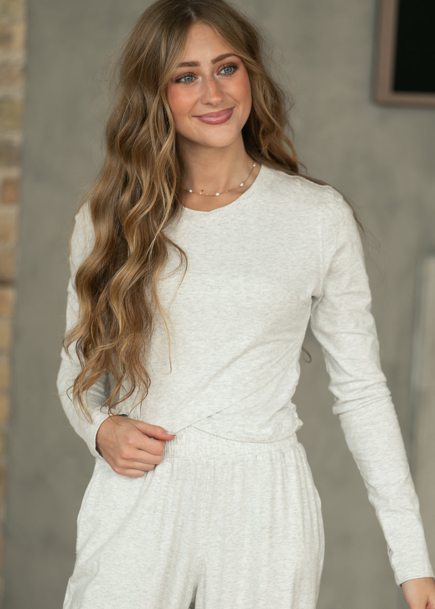 Close-up side view of heather gray long sleeve top showing fitted sleeves and crossover hem.
