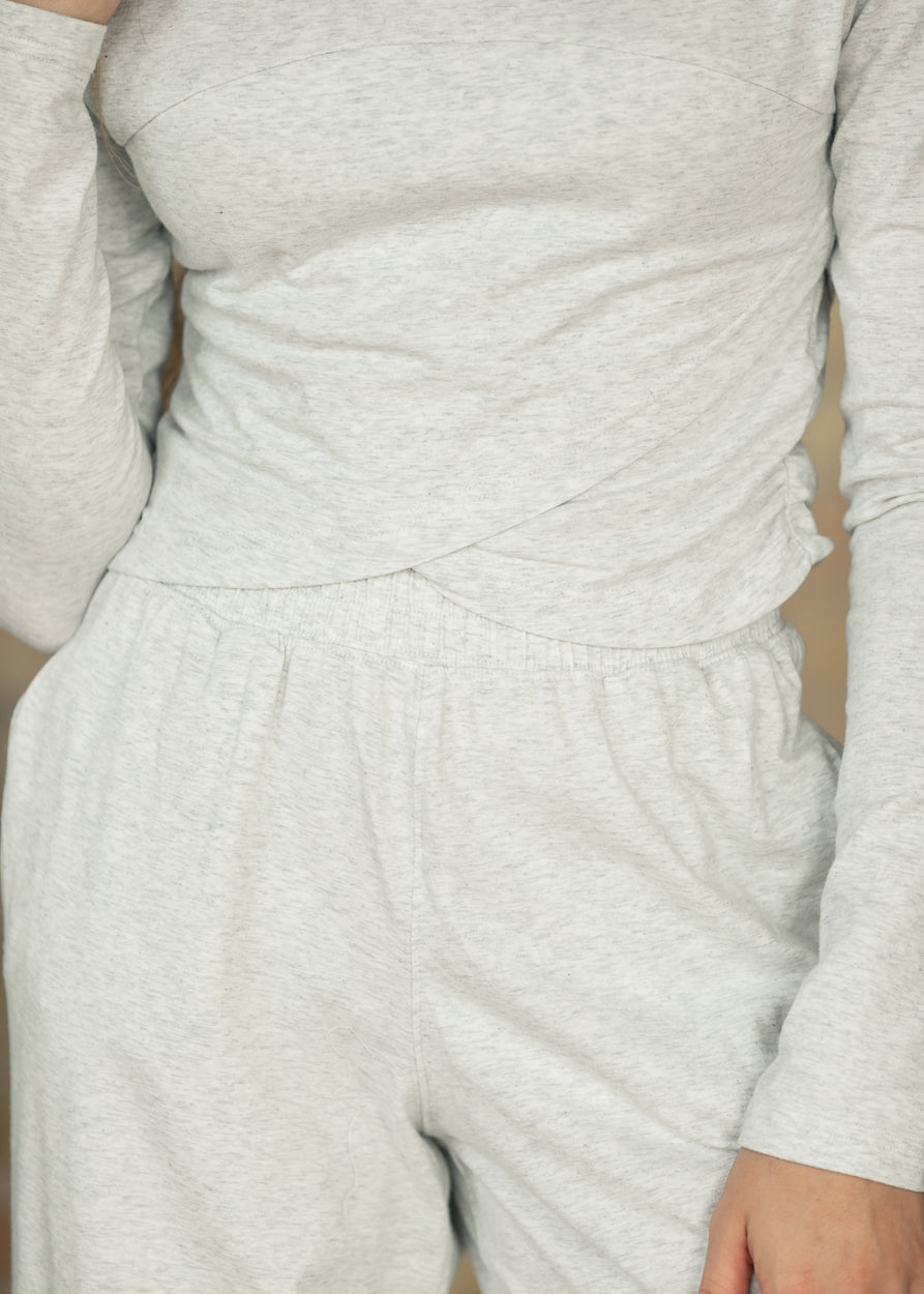 Close-up side view of heather gray long sleeve top showing fitted sleeves and crossover hem.