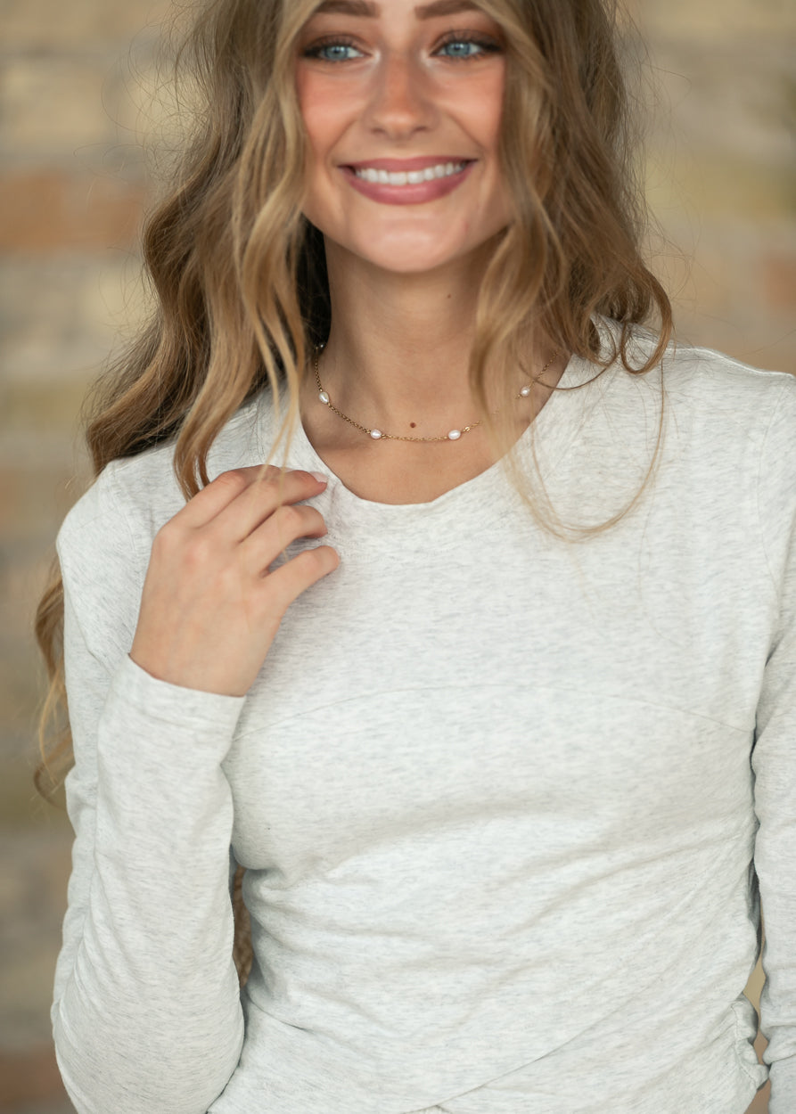 Close-up side view of heather gray long sleeve top showing fitted sleeves and crossover hem.