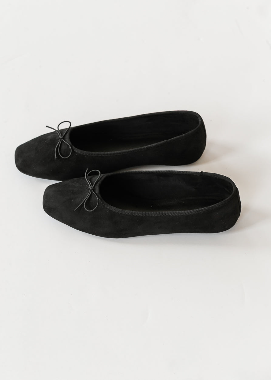 Side view of black velvety-soft ballet flats with delicate bow detail and low-profile silhouette.