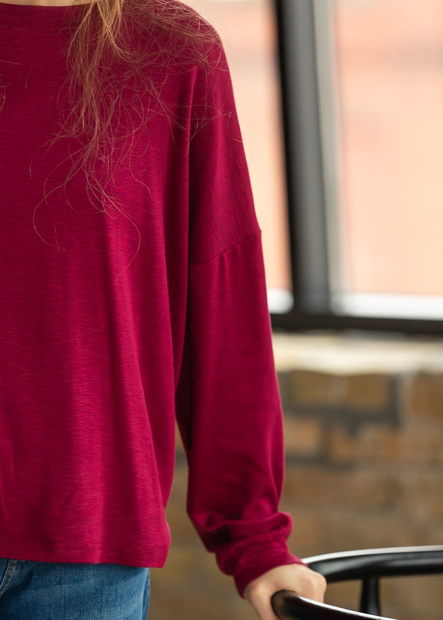 Maroon long sleeve top with a relaxed silhouette, styled with medium wash denim.
