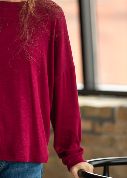 Maroon long sleeve top with a relaxed silhouette, styled with medium wash denim.