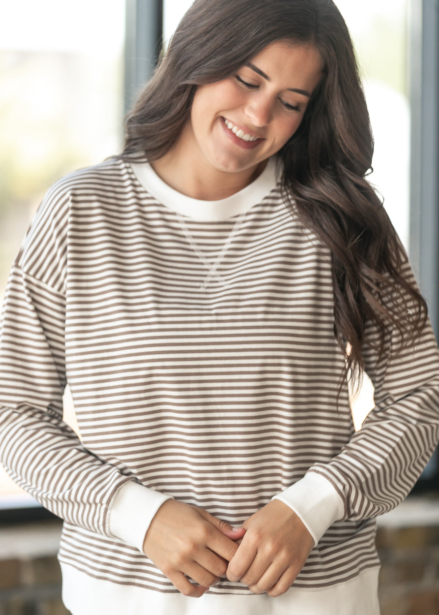 A woman wearing a beige and white horizontally striped long-sleeve crewneck shirt, smiling and looking down.