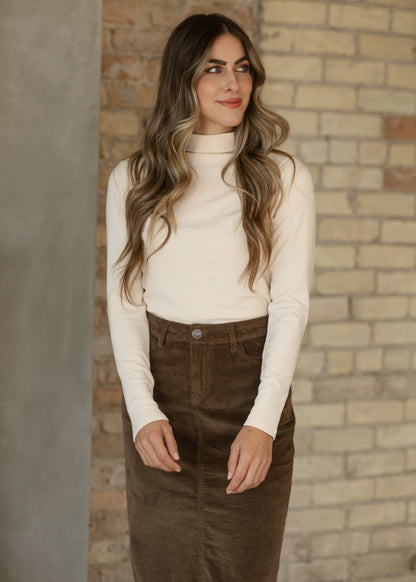 Ivory mock neck long sleeve top with a fitted silhouette, styled with a brown corduroy midi skirt.
