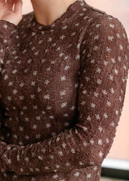 Close-up of brown floral textured fabric with lettuce trim at the neckline and cuffs.