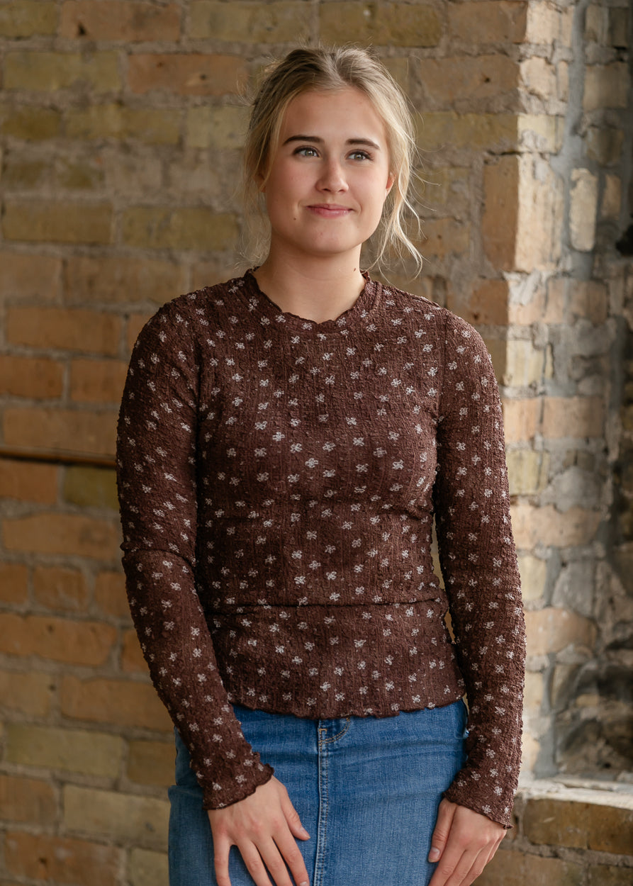 Brown floral long sleeve top with textured fabric, mock neckline, and delicate lettuce trim.