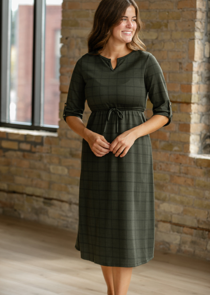 Monica olive windowpane dress showing its front waist tie, rolled sleeves, and below-the-knee hem.