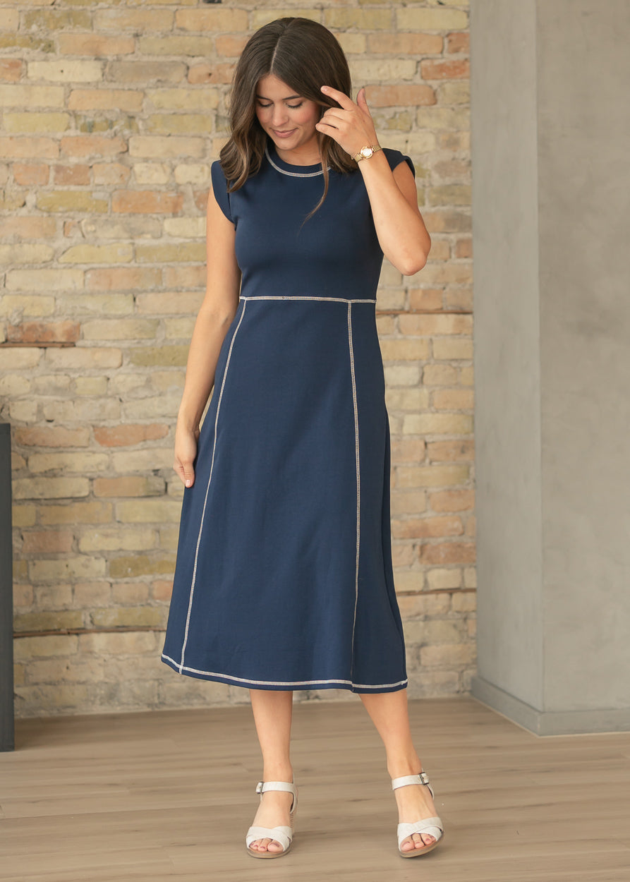 Navy contrast stitch midi dress with cap sleeves and side pockets styled with neutral heels.
